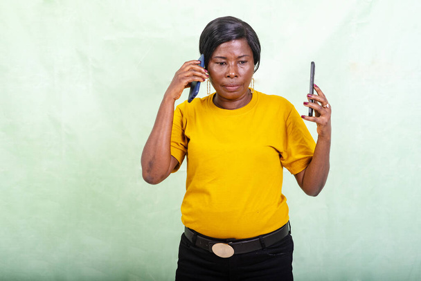 a beautiful woman in a yellow t-shirt standing on a green background talking on the cell phone. - Photo, Image