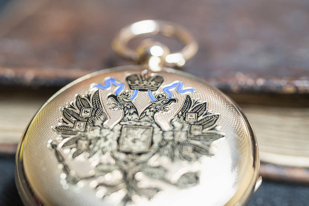 Χρυσό ρολόι τσέπης "Pavel Bure" σε χρυσό μενταγιόν. Βασιλική Ρωσία. ρολόι τσέπης σε σκούρο φόντο με βιβλία. Εικόνα από ένα χρυσό ρολόι τσέπης αντίκα σε ένα παλιό βιβλίο αντίκες. - Φωτογραφία, εικόνα