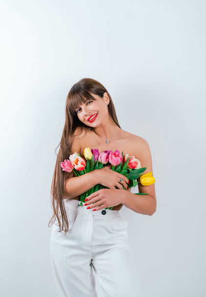 Ein schlankes Mädchen drückt ihr Blumen an die nackte Brust. Schöne Mädchen mit einem Strauß Tulpen isoliert auf weißem Hintergrund - Foto, Bild