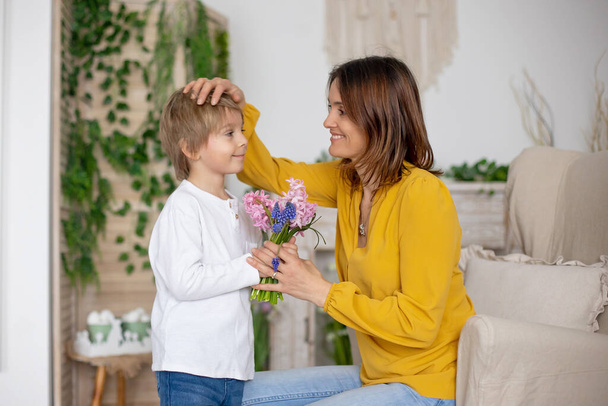 Cute little boy, giving flowers to his mom for Mothers day at home, cozy place - Zdjęcie, obraz