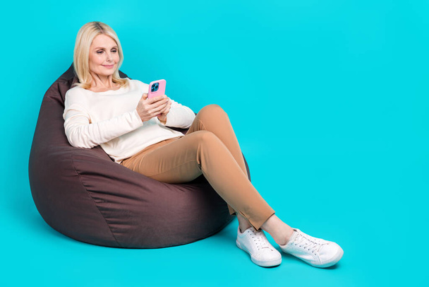 Full length photo of cute sweet lady dressed white shirt sitting bean bag texting device empty space isolated teal color background. - Foto, immagini