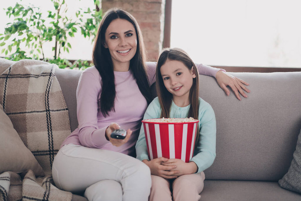 Photo of pretty mommy preteen daughter spend weekend together eat pop corn watch television sit comfortable sofa home flat. - Foto, Bild