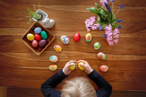 Little blond toddler boy child coloring easter eggs at home, Czech Republic tradition with twigs and eggs - Фото, изображение
