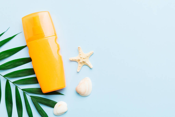 Sunscreen spray bottle. Bottle with sun protection cream and sea shells with tropical green leaf on color background, top view. - Fotoğraf, Görsel