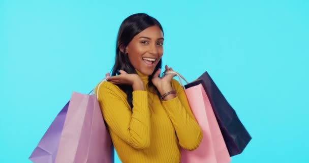 Šťastná žena, nákupní tašky a mrknutí ve studiu na nákup, prodej nebo slevu na modrém pozadí. Portrét ženského nakupujícího s úsměvem pro módu, nákupy nebo dárkové tašky v luxusu na maketě. - Záběry, video