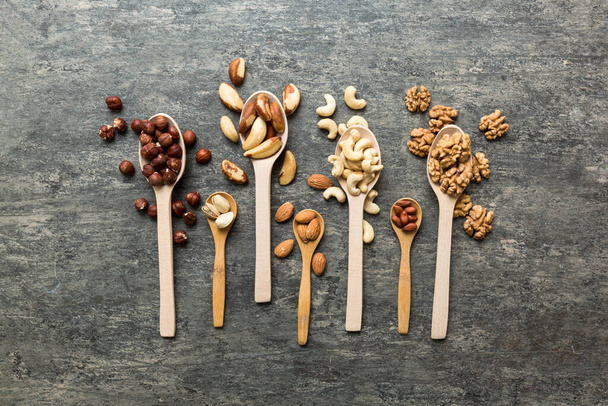 mixed nuts in white wooden spoon. Mix of various nuts on colored background. pistachios, cashews, walnuts, hazelnuts, peanuts and brazil nuts. - Valokuva, kuva