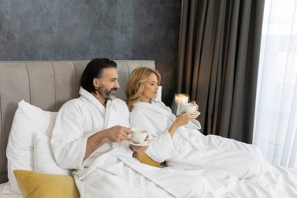 Красива пара в халаті в спальні п'є каву в ліжку
 - Фото, зображення