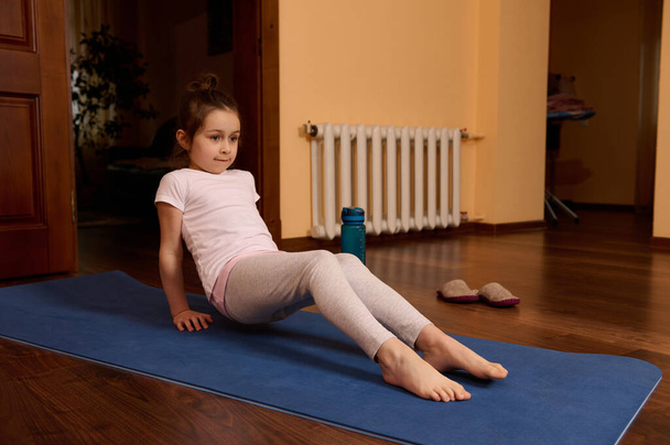 Caucasian active sporty little preschooler child girl in sportswear, exercising on a fitness mat indoors. Active lifestyle concept. Healthy habits. Hobby. Sport. People. Leisure activity. Childhood. - Photo, Image