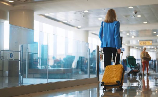 Женщина с чемоданом идет в терминал аэропорта. Вид сзади. - Фото, изображение