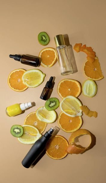 composition of variated bottles of serum of vitamin c and orange, lemon and green leaf flat lay on yellow background - Foto, afbeelding