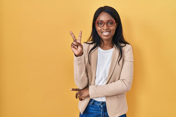 African young woman wearing glasses smiling with happy face winking at the camera doing victory sign. number two.  - Foto, afbeelding