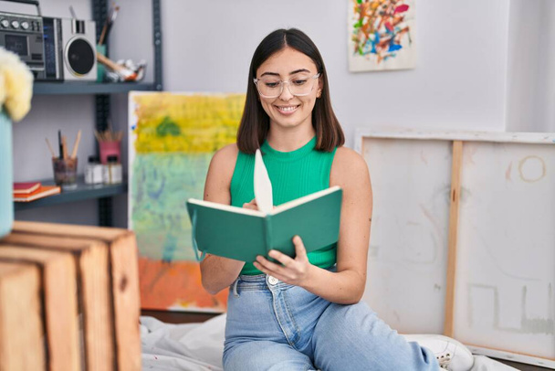 Νεαρή Ισπανίδα καλλιτέχνιδα διαβάζει βιβλία στο στούντιο τέχνης - Φωτογραφία, εικόνα