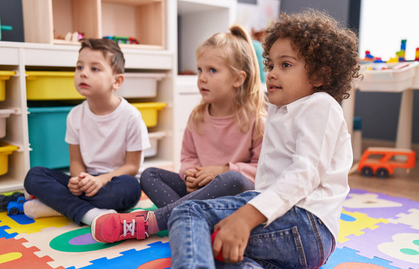 Grupa dzieci siedzących na podłodze z miłą ekspresją w przedszkolu - Zdjęcie, obraz