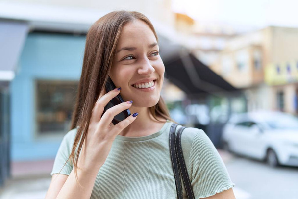 Νεαρή όμορφη γυναίκα χαμογελά αυτοπεποίθηση μιλώντας στο smartphone στο δρόμο - Φωτογραφία, εικόνα