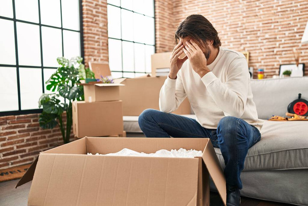 Middle age man unpacking cardboard box with worried expression at new home - Foto, immagini