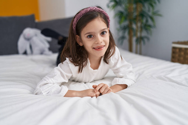 Schattig latino meisje glimlachen zelfverzekerd liggend op bed in de slaapkamer - Foto, afbeelding