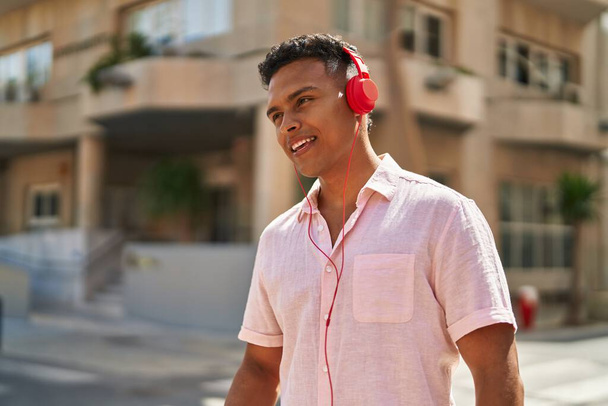 Nuori latinomies hymyilee luottavaisesti kuunnellen musiikkia kadulla - Valokuva, kuva