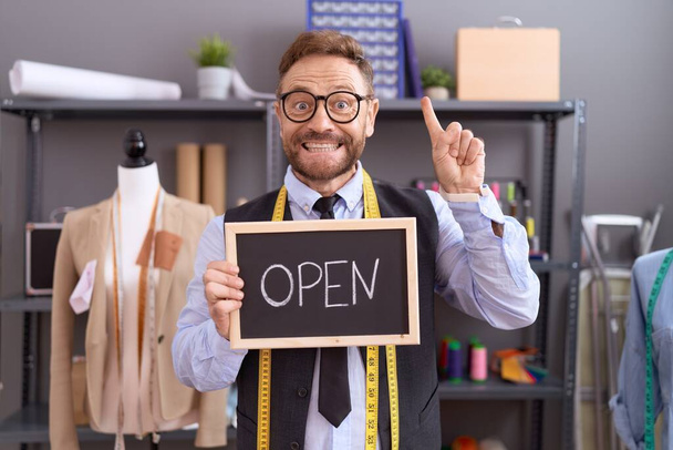 Middle age man with beard dressmaker designer holding open sign surprised with an idea or question pointing finger with happy face, number one  - Photo, Image