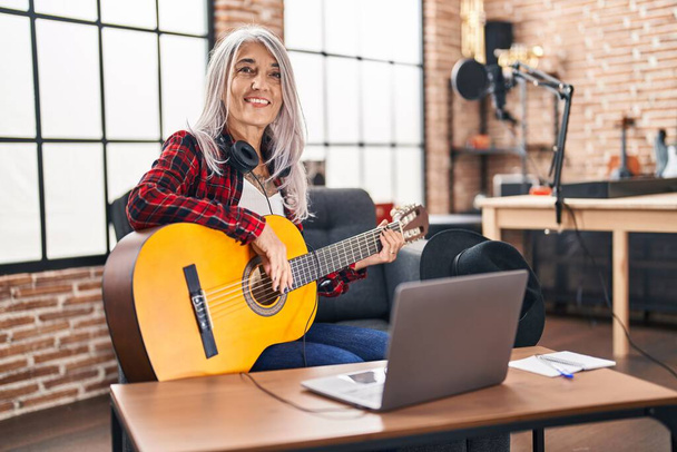 Mujer músico de pelo gris de mediana edad tocando guitarra clásica en el estudio de música - Foto, imagen