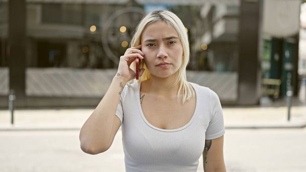 Junge schöne hispanische Frau spricht auf der Straße mit ernstem Gesichtsausdruck auf dem Smartphone - Foto, Bild