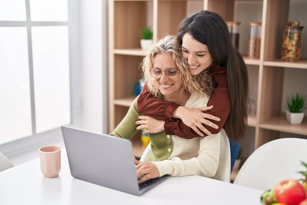 Δύο γυναίκες μητέρα και κόρη αγκαλιάζονται χρησιμοποιώντας φορητό υπολογιστή στο σπίτι - Φωτογραφία, εικόνα