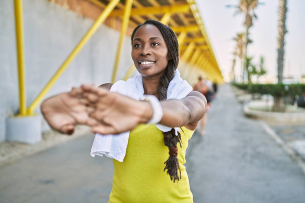 African american woman wearing sportswear stretching arm at street - 写真・画像