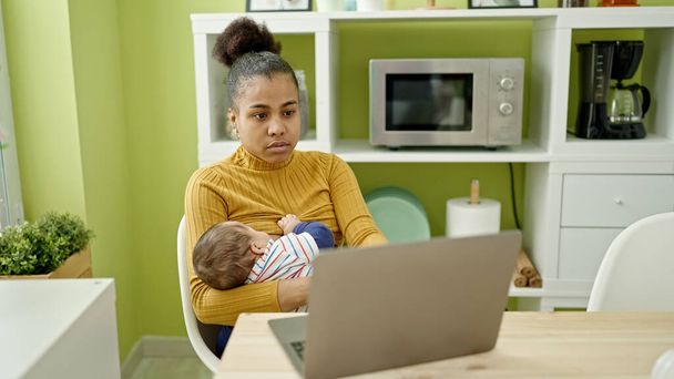 Madre e hijo trabajador de negocios que trabaja en línea mientras amamanta al bebé en el comedor - Foto, Imagen