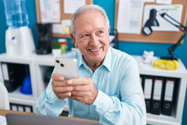 Trabajador de negocios hombre de pelo gris de mediana edad usando un teléfono inteligente que trabaja en la oficina - Foto, Imagen