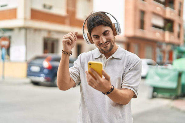 Junger hispanischer Mann lächelt selbstbewusst, hört Musik und tanzt auf der Straße - Foto, Bild