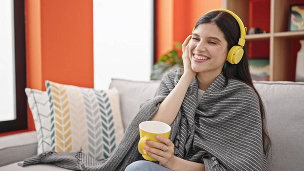 Joven mujer hispana hermosa escuchando música tomando café en casa - Foto, Imagen