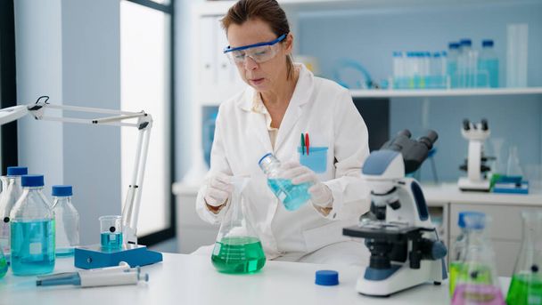 Keski-ikä latino nainen yllään tiedemies yhtenäinen kaatamalla nestettä koeputkeen laboratoriossa - Valokuva, kuva