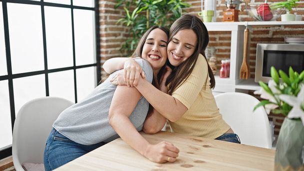 Two women hugging each other sitting on table at dinning room - Φωτογραφία, εικόνα