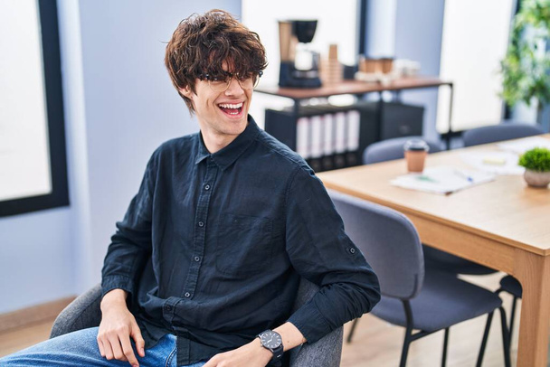 Young hispanic man business worker smiling confident sitting on chair at office - 写真・画像