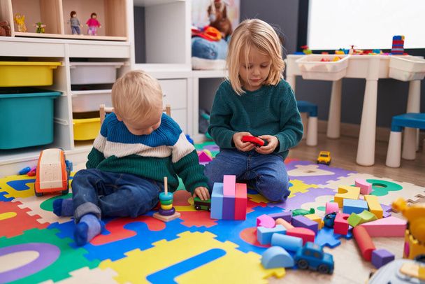 Adorable boy and girl playing with construction blocks sitting on floor at kindergarten - 写真・画像