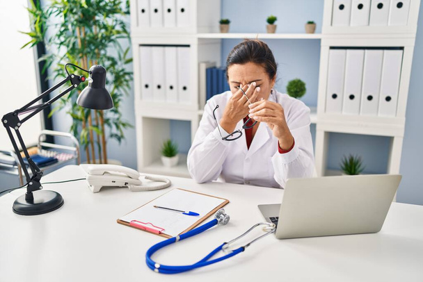 Middle age hispanic woman wearing doctor uniform stressed working at clinic - Fotoğraf, Görsel