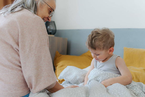 Grandmother giving her grandson in a bed. - Fotó, kép