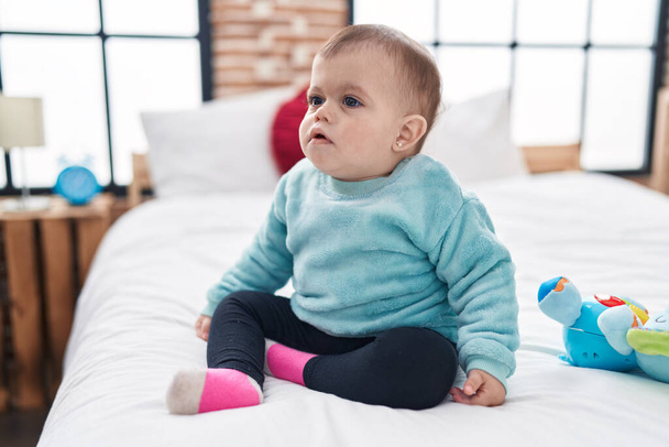 Imádnivaló spanyol baba ül az ágyon nyugodt kifejezés a hálószobában - Fotó, kép