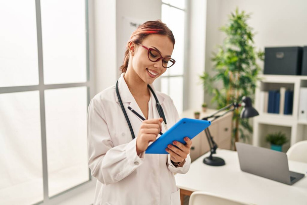 Νεαρή καυκάσια γυναίκα γιατρός χρησιμοποιώντας touchpad στέκεται στην κλινική - Φωτογραφία, εικόνα