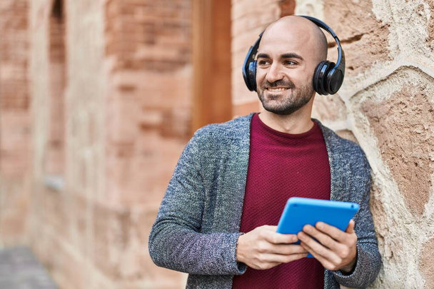 Junger Mann lächelt selbstbewusst mit Touchpad und Kopfhörer auf der Straße - Foto, Bild