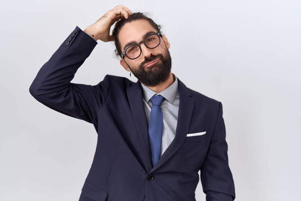 Hispanic man with beard wearing suit and tie confuse and wonder about question. uncertain with doubt, thinking with hand on head. pensive concept.  - Photo, Image
