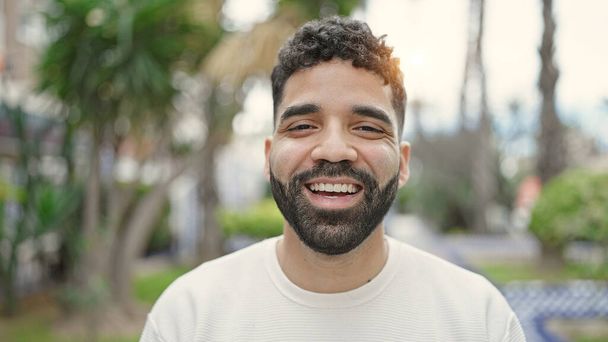 Joven hombre hispano sonriendo confiado de pie en el parque - Foto, imagen