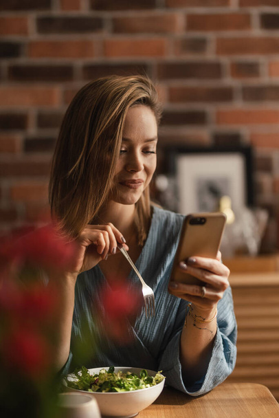 Young woman eating vegetable salad and scrolling her phone. - Foto, immagini