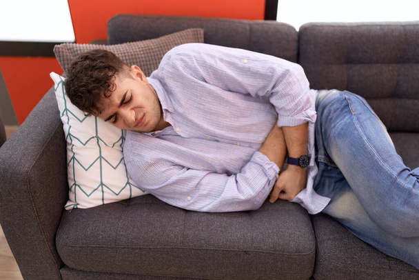 Fiatal spanyol férfi szenved gyomorfájás feküdt kanapén otthon - Fotó, kép