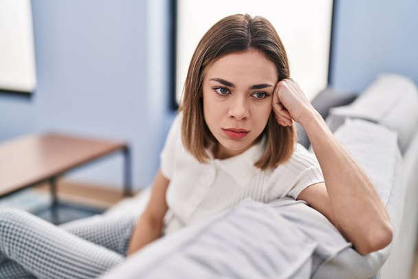 Young beautiful hispanic woman sitting on sofa with serious expression at home - Photo, Image