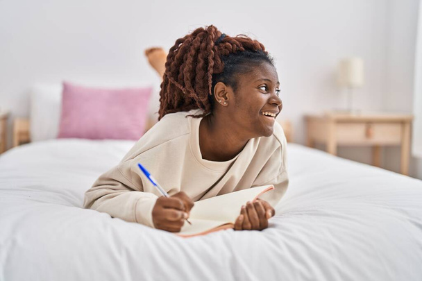 Donna afroamericana che scrive sul taccuino sdraiato sul letto in camera da letto - Foto, immagini