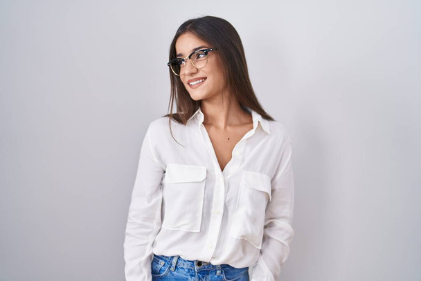 Jeune femme brune portant des lunettes regardant de côté avec le sourire sur le visage, expression naturelle. riant confiant.  - Photo, image