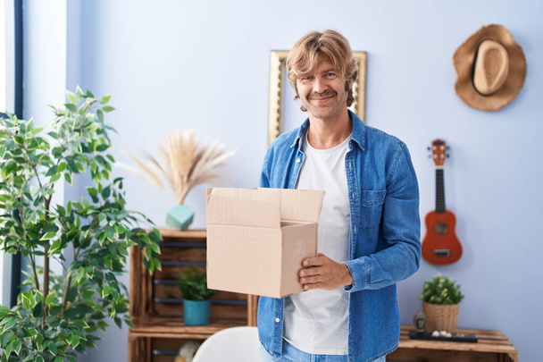 Young man smiling confident holding package at home - Photo, Image