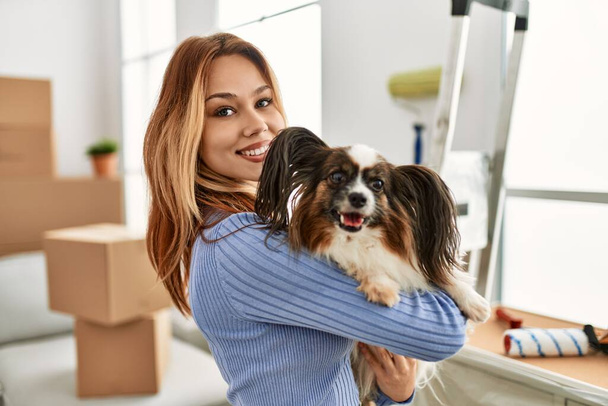 Молодая белая женщина улыбается уверенно обнимая собаку в новом доме - Фото, изображение