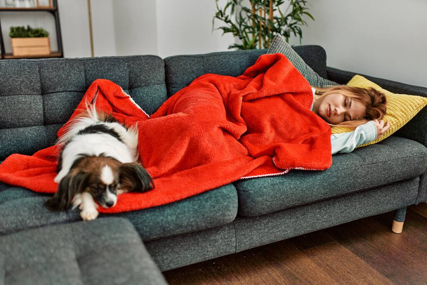 Young caucasian woman lying on sofa sleeping with dog at home - Photo, image