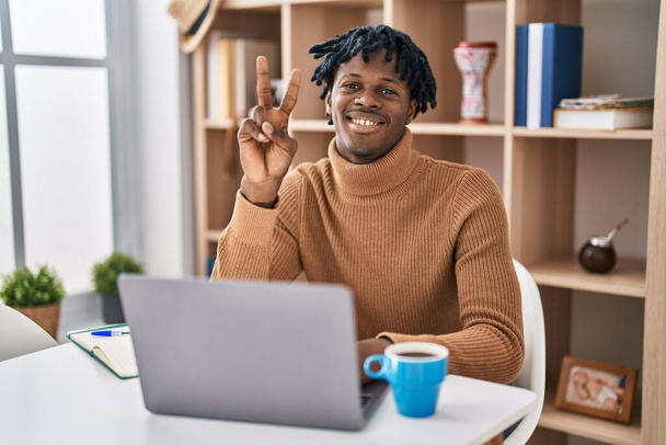 Fiatal afrikai férfi raszta dolgozik számítógépes laptop mutatja, és rámutatva ujjak száma 2, miközben mosolygós magabiztos és boldog.  - Fotó, kép
